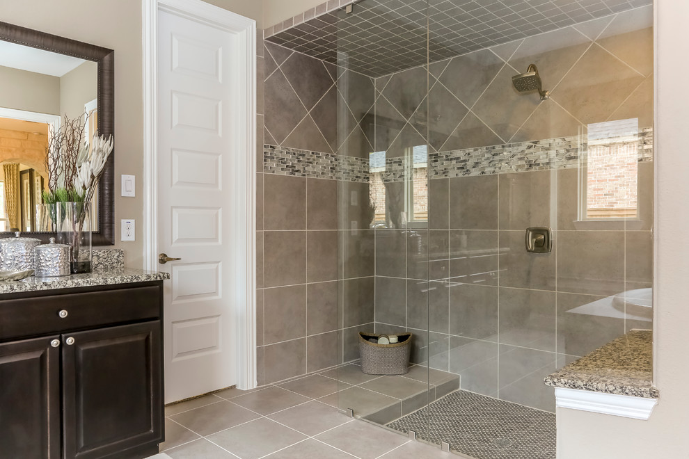 This is an example of a large master bathroom in Houston with raised-panel cabinets, black cabinets, a drop-in tub, a double shower, gray tile, glass tile, beige walls, porcelain floors, an undermount sink and granite benchtops.
