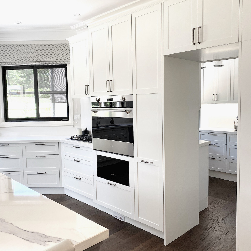 Photo of a large traditional u-shaped kitchen in Sydney with a double-bowl sink, shaker cabinets, white cabinets, engineered stone countertops, white splashback, engineered quartz splashback, stainless steel appliances, dark hardwood flooring, an island, brown floors and white worktops.