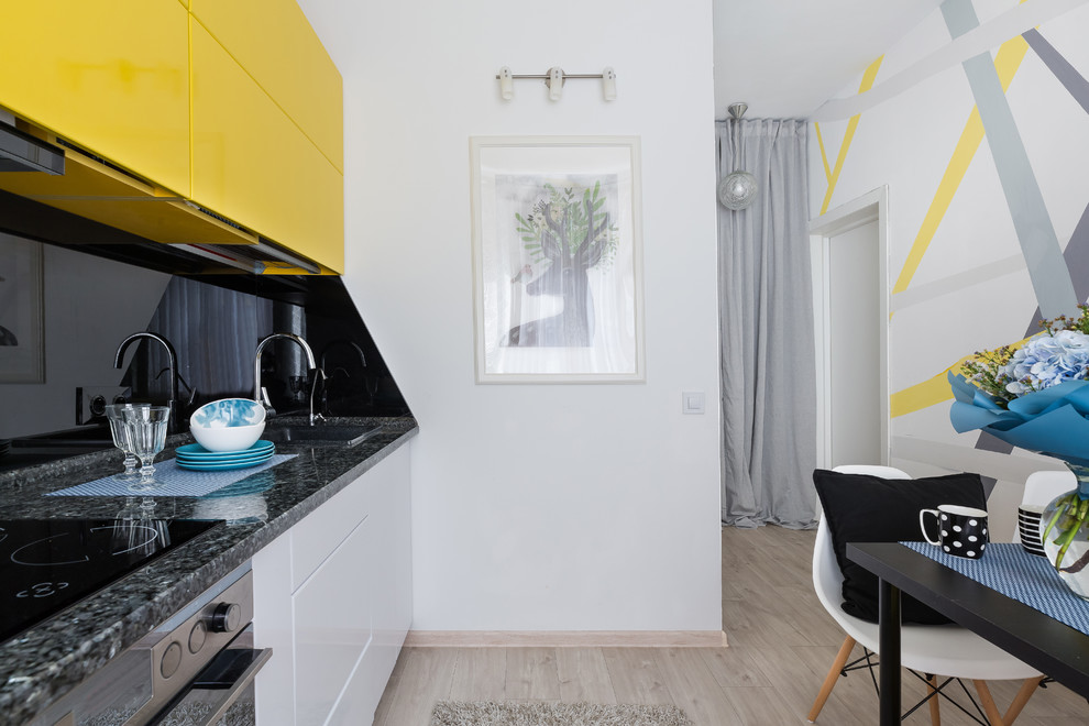 Inspiration for a small single-wall eat-in kitchen in Saint Petersburg with a drop-in sink, flat-panel cabinets, yellow cabinets, solid surface benchtops, black splashback, glass sheet splashback, stainless steel appliances, laminate floors, no island, beige floor and black benchtop.