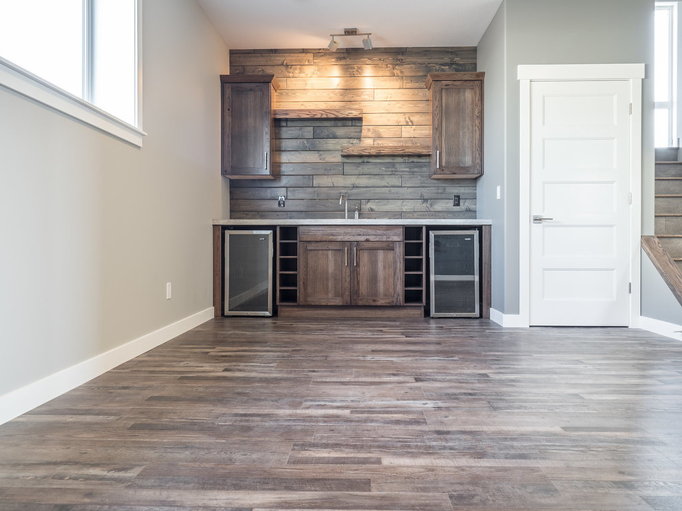 Photo of a mid-sized country single-wall wet bar in Edmonton with a drop-in sink, recessed-panel cabinets, brown cabinets, quartzite benchtops, multi-coloured splashback, timber splashback, vinyl floors and grey floor.