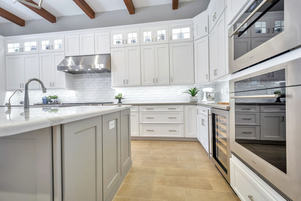 Large transitional u-shaped separate kitchen in Phoenix with a farmhouse sink, shaker cabinets, white cabinets, quartz benchtops, white splashback, glass tile splashback, stainless steel appliances, porcelain floors, with island, beige floor, white benchtop and exposed beam.