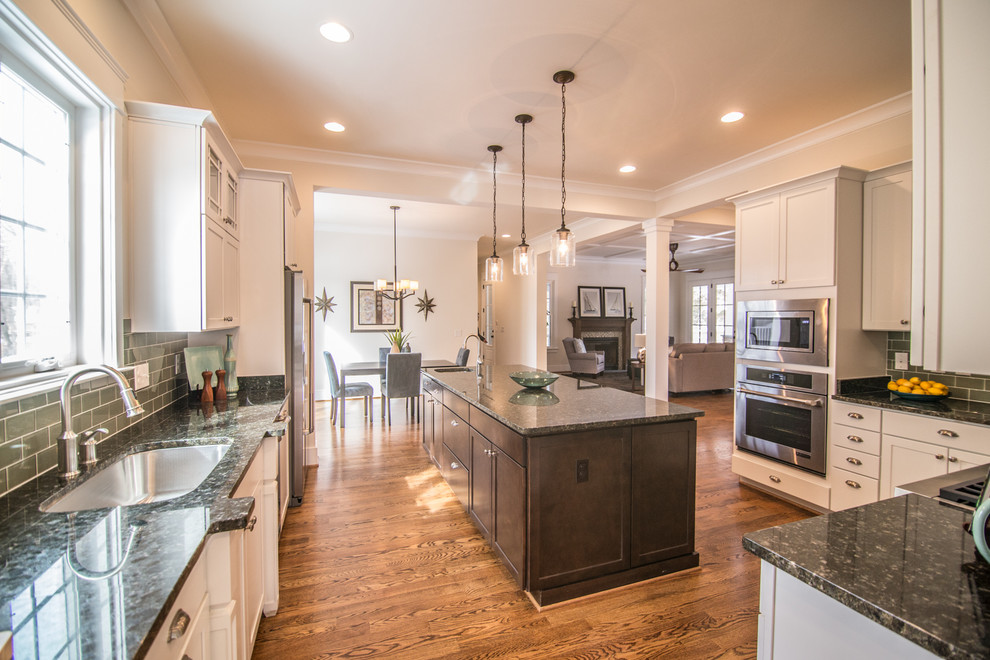 Example of an u-shaped dark wood floor eat-in kitchen design in DC Metro with an undermount sink, shaker cabinets, granite countertops, green backsplash, glass tile backsplash, stainless steel appliances and an island