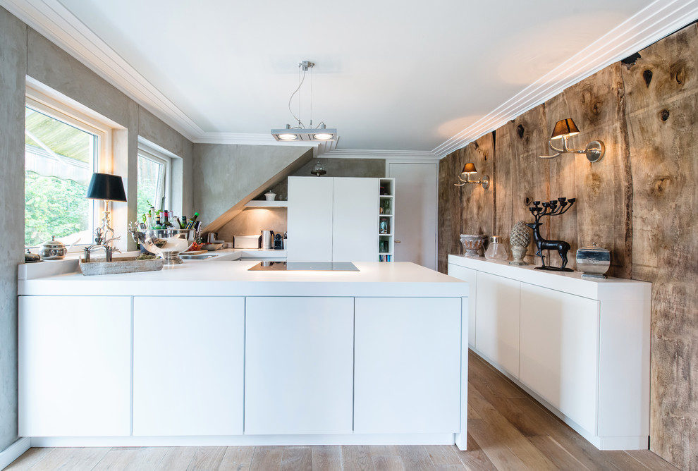 This is an example of a mid-sized contemporary u-shaped open plan kitchen in Berlin with flat-panel cabinets, white cabinets, grey splashback, medium hardwood floors, a peninsula and a drop-in sink.