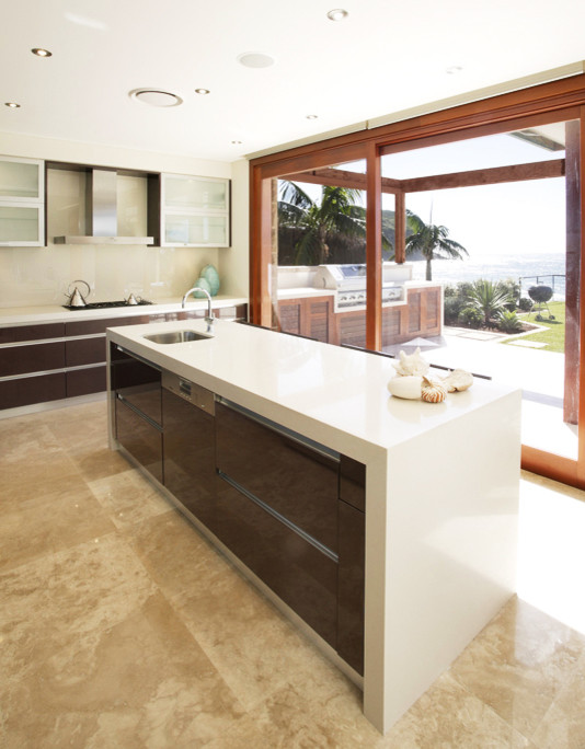 Design ideas for a mid-sized contemporary l-shaped eat-in kitchen in Sydney with an undermount sink, flat-panel cabinets, brown cabinets, quartzite benchtops, beige splashback, glass sheet splashback, stainless steel appliances, limestone floors and with island.