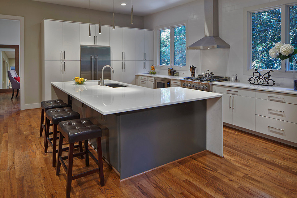 Photo of a large modern l-shaped eat-in kitchen in Atlanta with an undermount sink, flat-panel cabinets, white cabinets, quartz benchtops, white splashback, subway tile splashback, stainless steel appliances, medium hardwood floors and with island.