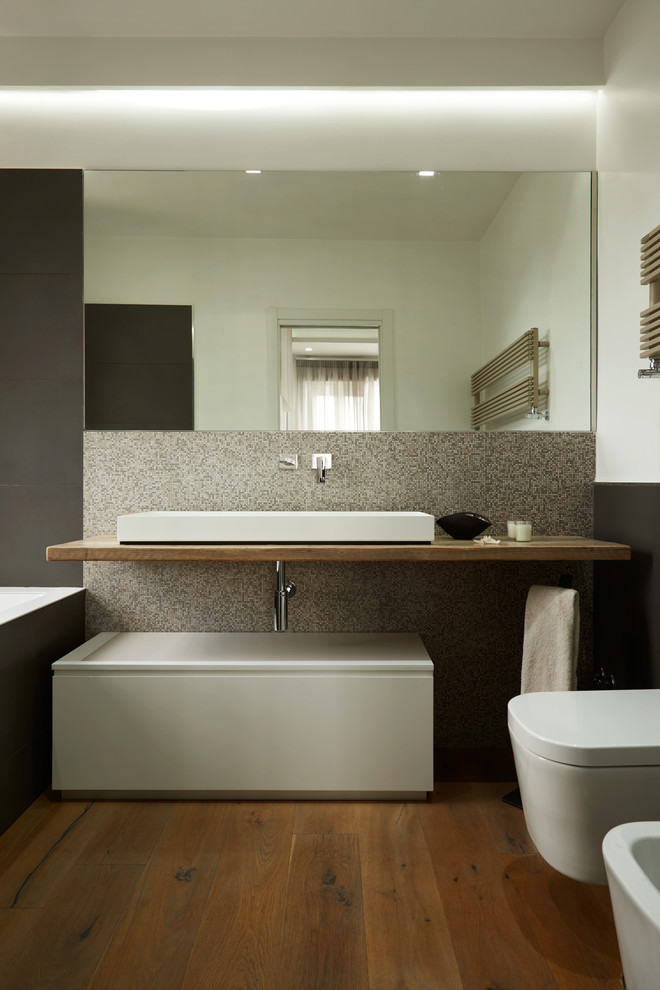 Photo of a modern master bathroom in Rome with light wood cabinets, a drop-in tub, a two-piece toilet, beige tile, mosaic tile, medium hardwood floors, a trough sink, wood benchtops and brown floor.
