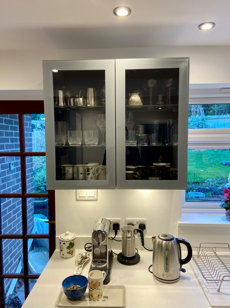 Mid-sized modern l-shaped separate kitchen in Sussex with a drop-in sink, flat-panel cabinets, blue cabinets, quartzite benchtops, white splashback, ceramic splashback, black appliances, vinyl floors, no island, brown floor and white benchtop.