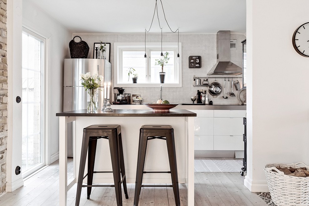 Inspiration for a small scandinavian galley kitchen in Malmo with flat-panel cabinets, white cabinets, white splashback, light hardwood floors, with island, beige floor, stainless steel benchtops and stainless steel appliances.