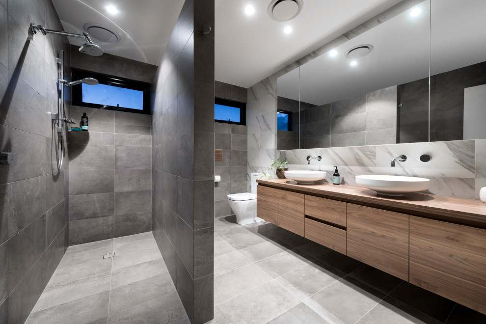 This is an example of a large contemporary master bathroom in Perth with flat-panel cabinets, medium wood cabinets, a corner shower, a one-piece toilet, gray tile, a vessel sink, wood benchtops, grey floor, an open shower, brown benchtops, a double vanity and a floating vanity.