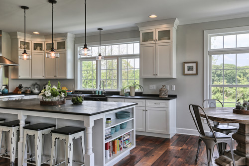 Bright farmhouse kitchen with white shaker kitchen cabinet layout, large island with open shelves, black countertops, and rustic wood flooring.