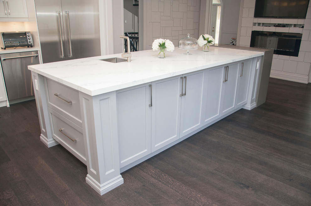 Large transitional l-shaped dark wood floor and brown floor enclosed kitchen photo in Toronto with an undermount sink, shaker cabinets, white cabinets, quartz countertops, white backsplash, marble backsplash, stainless steel appliances, an island and white countertops
