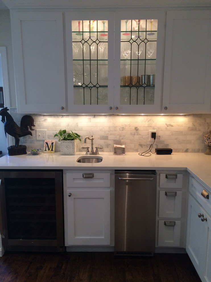 Mid-sized transitional u-shaped dark wood floor eat-in kitchen photo with a farmhouse sink, shaker cabinets, white cabinets, quartzite countertops, white backsplash, stone tile backsplash, stainless steel appliances and an island