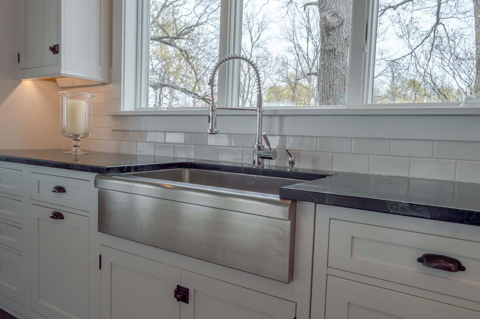 Expansive traditional l-shaped kitchen pantry in New York with a farmhouse sink, recessed-panel cabinets, white cabinets, marble benchtops, white splashback, ceramic splashback, stainless steel appliances, dark hardwood floors, with island and brown floor.