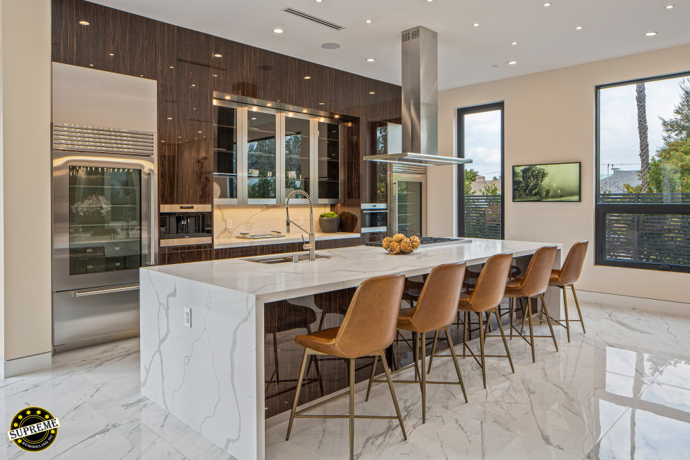 This is an example of a large modern single-wall open plan kitchen in Los Angeles with an undermount sink, flat-panel cabinets, dark wood cabinets, marble benchtops, white splashback, marble splashback, stainless steel appliances, marble floors, with island, white floor and white benchtop.