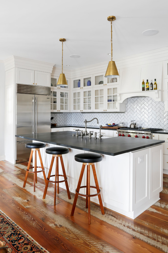 Photo of a country l-shaped kitchen in Nashville with a farmhouse sink, glass-front cabinets, white cabinets, white splashback, subway tile splashback, medium hardwood floors, with island and brown floor.
