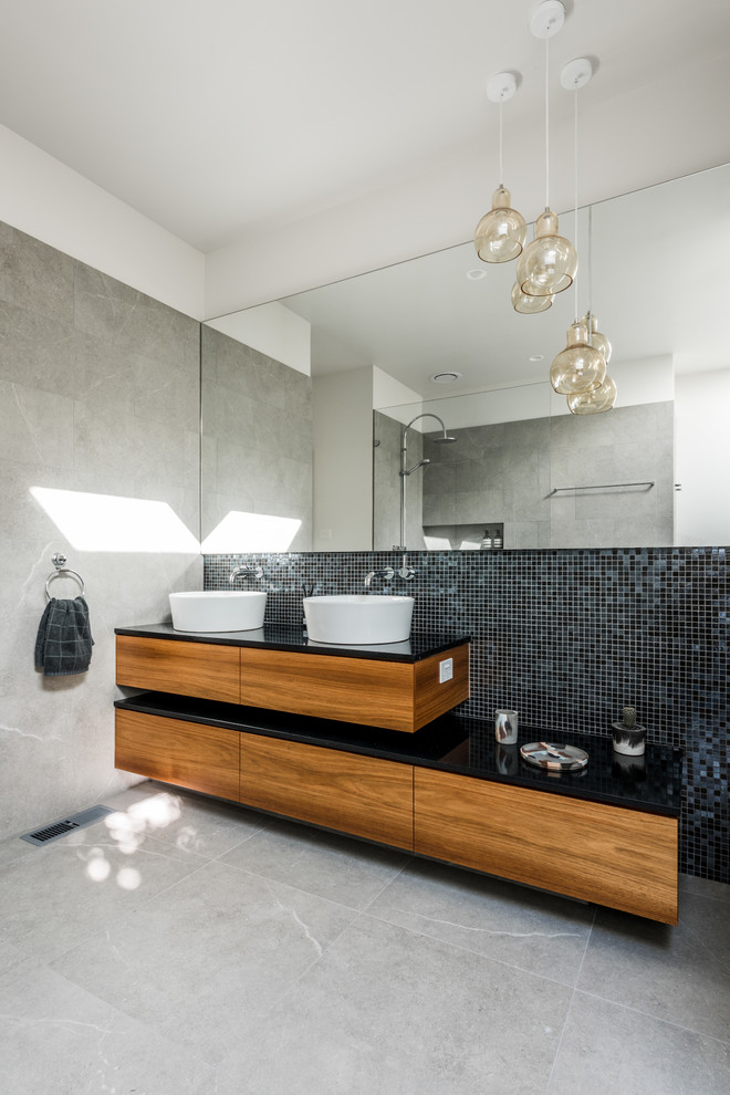 Photo of a contemporary master bathroom in Melbourne with an open shower, ceramic floors, a vessel sink, flat-panel cabinets, medium wood cabinets, black tile, mosaic tile, white walls and an open shower.