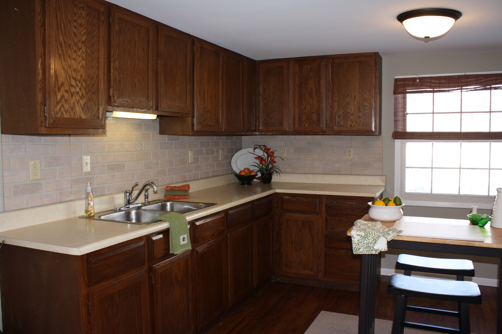 This is an example of a mid-sized traditional u-shaped separate kitchen in Milwaukee with a double-bowl sink, raised-panel cabinets, dark wood cabinets, laminate benchtops, pink splashback, brick splashback, white appliances, medium hardwood floors and with island.