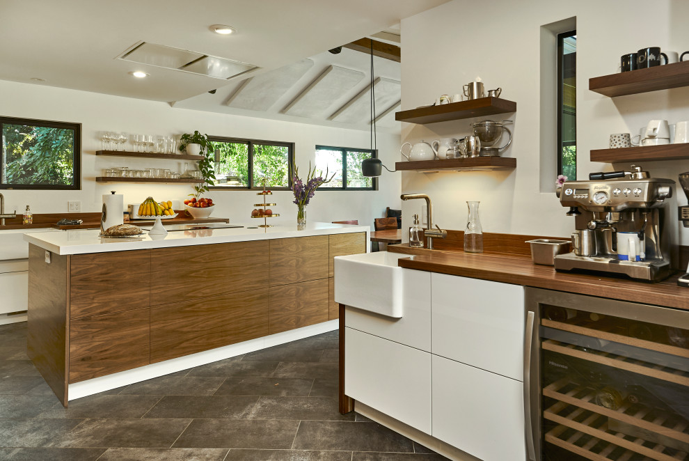 Design ideas for a mid-sized midcentury l-shaped eat-in kitchen in San Francisco with a farmhouse sink, medium wood cabinets, wood benchtops, brown splashback, timber splashback, panelled appliances, porcelain floors, with island, grey floor, white benchtop and vaulted.