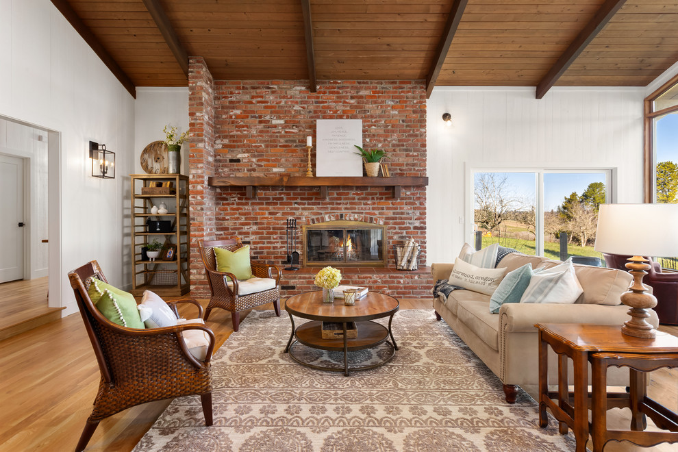 Photo of a country open concept living room in Portland with white walls, light hardwood floors, a standard fireplace, a brick fireplace surround and beige floor.