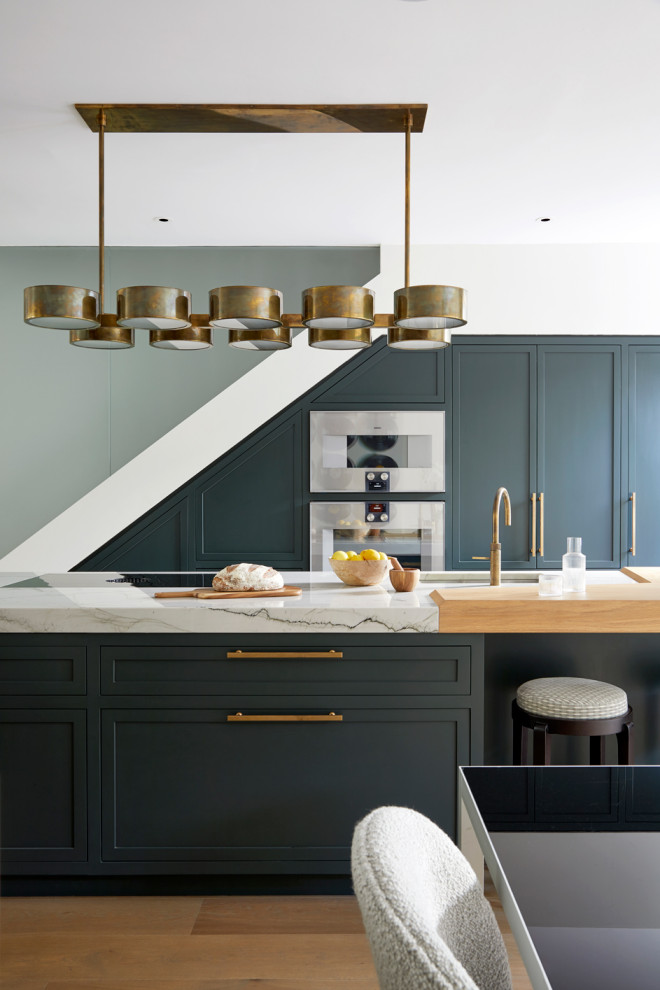 This is an example of a mid-sized transitional single-wall open plan kitchen in London with shaker cabinets, green cabinets, marble benchtops, stainless steel appliances, with island and multi-coloured benchtop.