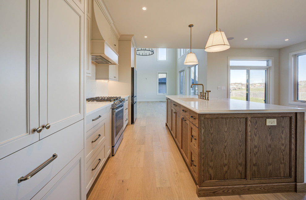 Open concept kitchen - mid-sized transitional single-wall light wood floor open concept kitchen idea in Toronto with an undermount sink, shaker cabinets, medium tone wood cabinets, quartz countertops, white backsplash, quartz backsplash, stainless steel appliances, an island and white countertops