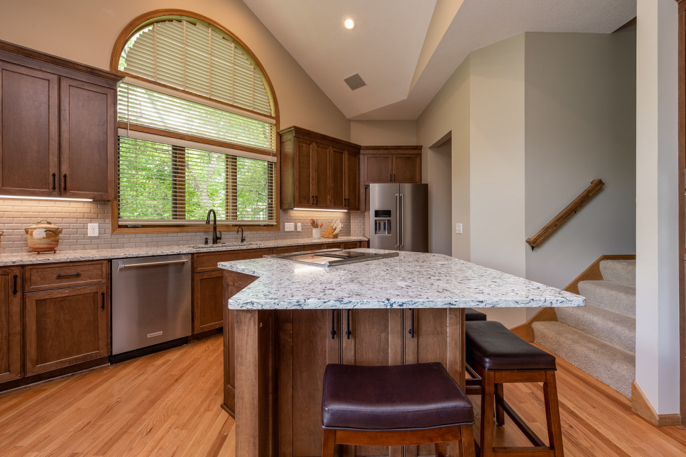 Design ideas for a traditional open plan kitchen in Minneapolis with a drop-in sink, flat-panel cabinets, medium wood cabinets, quartz benchtops, beige splashback, porcelain splashback, stainless steel appliances, medium hardwood floors, with island, beige benchtop and vaulted.