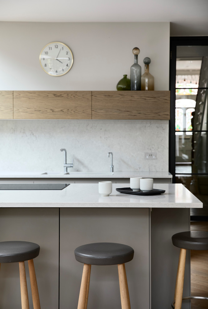 Photo of a contemporary kitchen/diner in Other with a double-bowl sink, flat-panel cabinets, beige cabinets, engineered stone countertops, white splashback, engineered quartz splashback, black appliances, light hardwood flooring, an island, beige floors and white worktops.