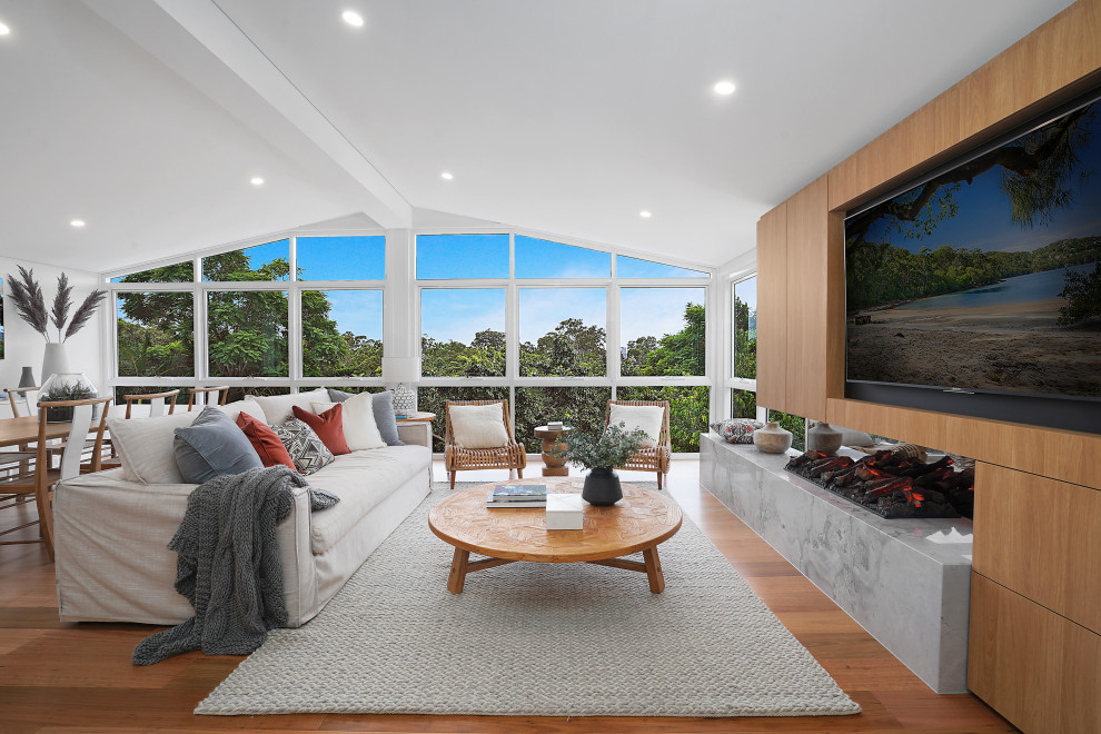 This is an example of a large contemporary open concept living room in Brisbane with white walls, a two-sided fireplace, a wood fireplace surround, a built-in media wall and brown floor.