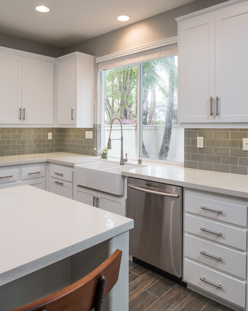 Mid-sized modern u-shaped kitchen in San Diego with a farmhouse sink, shaker cabinets, white cabinets, quartz benchtops, grey splashback, subway tile splashback, stainless steel appliances, plywood floors and with island.