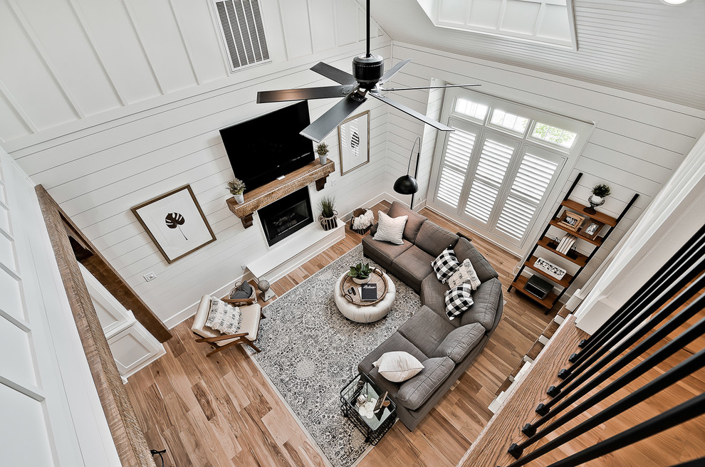 This is an example of a large arts and crafts open concept family room in Other with white walls, light hardwood floors, a standard fireplace, a wood fireplace surround and a wall-mounted tv.