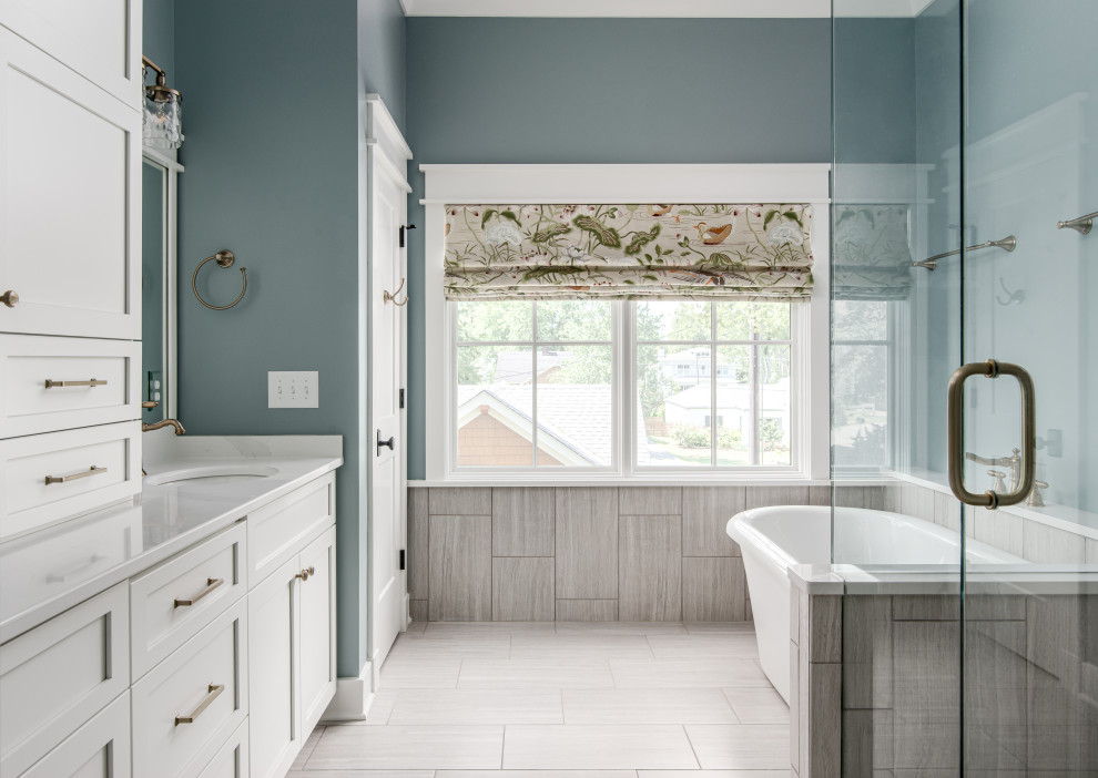 Photo of a mid-sized transitional master bathroom in Nashville with shaker cabinets, white cabinets, a freestanding tub, an alcove shower, gray tile, porcelain tile, blue walls, porcelain floors, an undermount sink, engineered quartz benchtops, grey floor, a hinged shower door, white benchtops, an enclosed toilet, a double vanity and a built-in vanity.