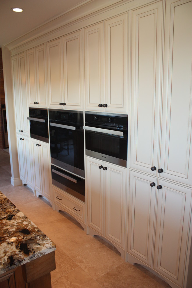 Inspiration for a mid-sized rustic l-shaped porcelain tile and beige floor kitchen pantry remodel in Vancouver with an undermount sink, raised-panel cabinets, white cabinets, granite countertops, beige backsplash, ceramic backsplash, stainless steel appliances and an island