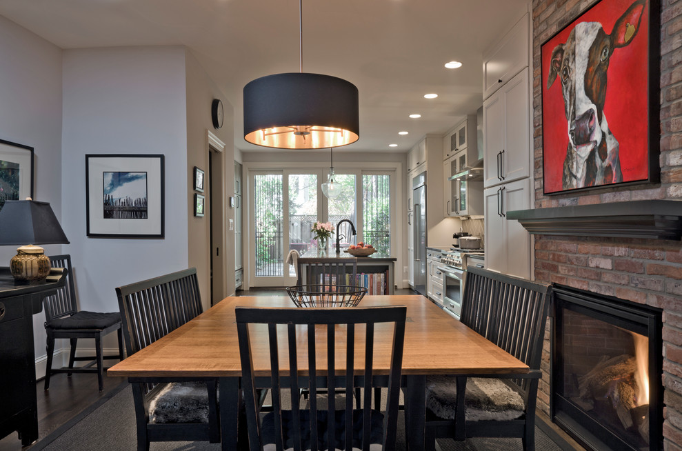 Cette image montre une salle à manger ouverte sur la cuisine design de taille moyenne avec un mur gris, parquet foncé, une cheminée standard, un manteau de cheminée en brique, un sol marron et un mur en parement de brique.