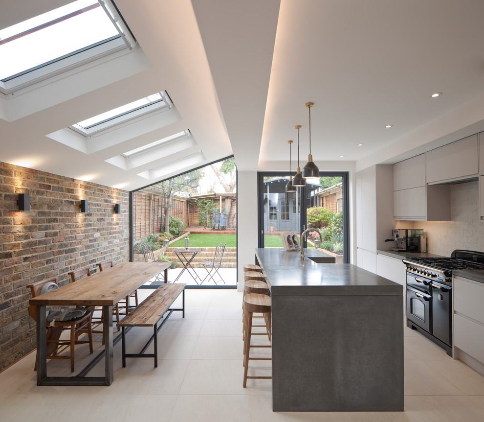 This is an example of a mid-sized contemporary single-wall eat-in kitchen in London with flat-panel cabinets, grey cabinets, concrete benchtops, white splashback, brick splashback, black appliances, with island and white floor.