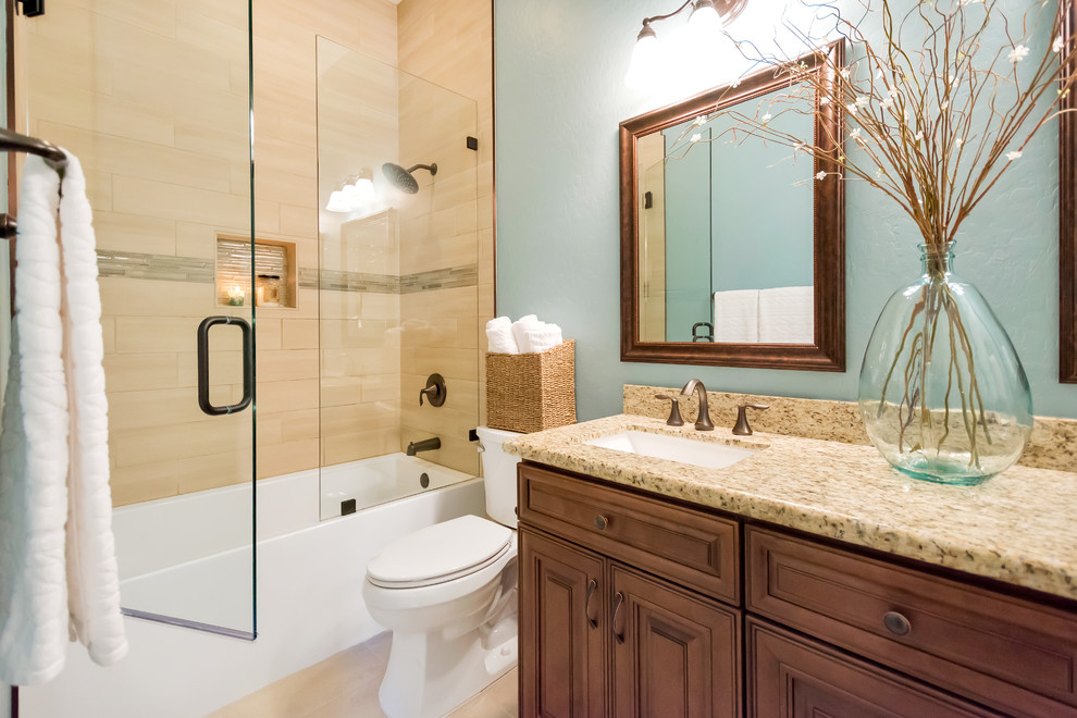 Drop-in bathtub - mid-sized transitional kids' beige tile and porcelain tile porcelain tile and beige floor drop-in bathtub idea in Phoenix with brown cabinets, blue walls, an undermount sink, granite countertops, raised-panel cabinets, a two-piece toilet and a hinged shower door