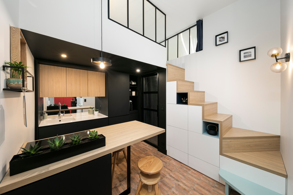 Contemporary open plan kitchen in Rennes with flat-panel cabinets, black cabinets, panelled appliances, brick floors, a peninsula and white benchtop.