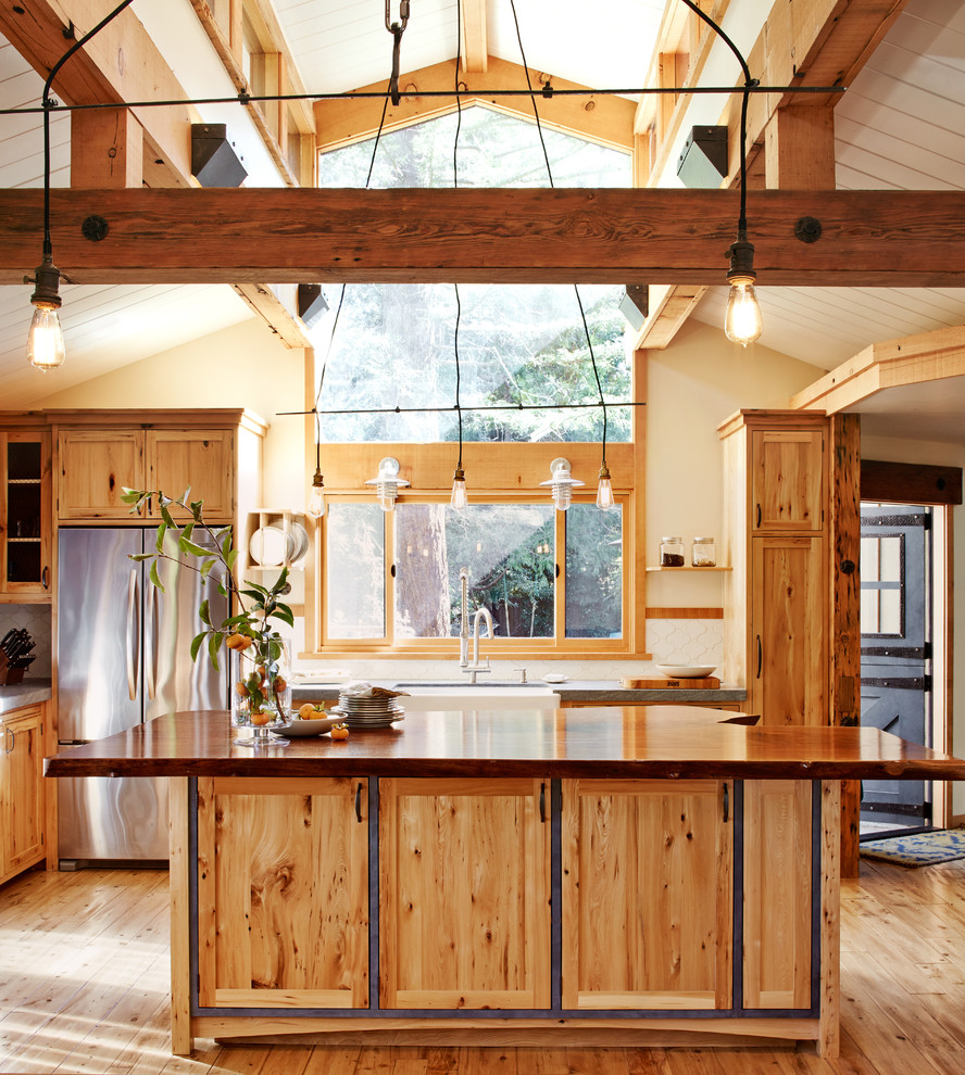 Photo of a country l-shaped eat-in kitchen in San Francisco with a farmhouse sink, shaker cabinets, medium wood cabinets, white splashback, stainless steel appliances, light hardwood floors and with island.