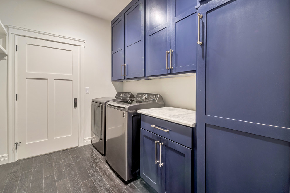 Photo of a large transitional single-wall dedicated laundry room in Salt Lake City with shaker cabinets, blue cabinets, marble benchtops, beige walls, dark hardwood floors, a side-by-side washer and dryer, brown floor and white benchtop.