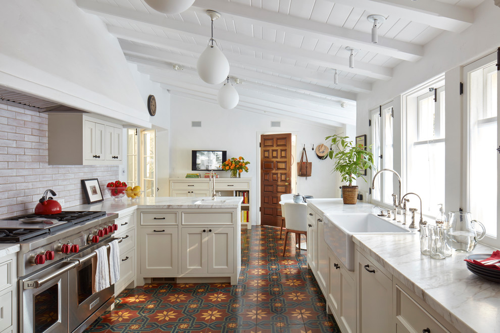 This is an example of a mediterranean u-shaped eat-in kitchen in Los Angeles with a farmhouse sink, shaker cabinets, beige cabinets, stainless steel appliances, ceramic floors, a peninsula, red floor, white benchtop and subway tile splashback.