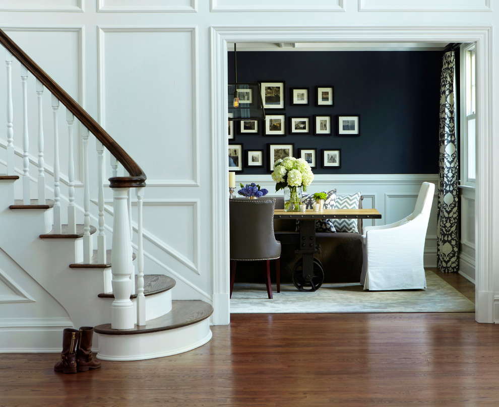 This is an example of a transitional dining room in New York with black walls and dark hardwood floors.