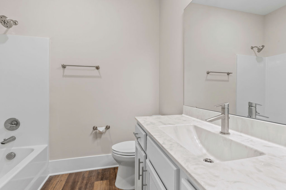 This is an example of a large traditional bathroom in Raleigh with recessed-panel cabinets, white cabinets, an alcove tub, a shower/bathtub combo, a two-piece toilet, gray tile, beige walls, vinyl floors, an integrated sink, marble benchtops, brown floor, a shower curtain, white benchtops, a single vanity and a built-in vanity.