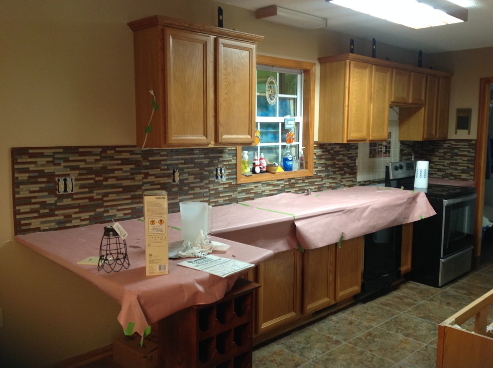 Inspiration for a l-shaped eat-in kitchen remodel with an undermount sink, flat-panel cabinets, brown backsplash, glass tile backsplash, stainless steel appliances and a peninsula