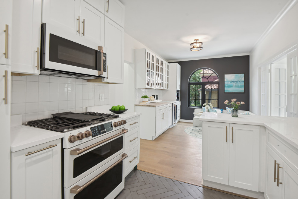 Modern galley kitchen/diner in DC Metro with a submerged sink, shaker cabinets, white cabinets, engineered stone countertops, white splashback, ceramic splashback, white appliances, ceramic flooring, a breakfast bar, grey floors and white worktops.