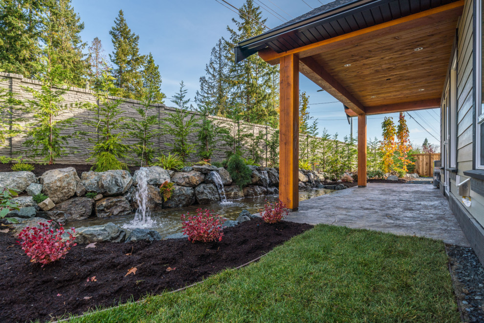 This is an example of a contemporary backyard patio in Vancouver with a water feature, stamped concrete and a roof extension.