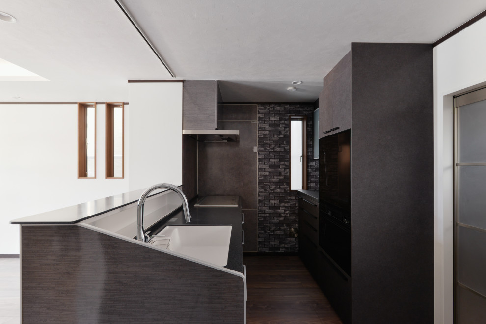 This is an example of a small contemporary kitchen in Other with an integrated sink, recessed-panel cabinets, grey cabinets, solid surface benchtops, grey splashback, engineered quartz splashback, black appliances, painted wood floors, a peninsula, brown floor, brown benchtop and recessed.