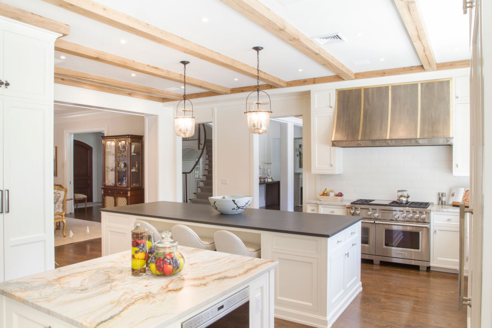 This is an example of a large transitional l-shaped eat-in kitchen in New York with shaker cabinets, white cabinets, quartz benchtops, white splashback, engineered quartz splashback, painted wood floors, multiple islands, brown floor, black benchtop and exposed beam.