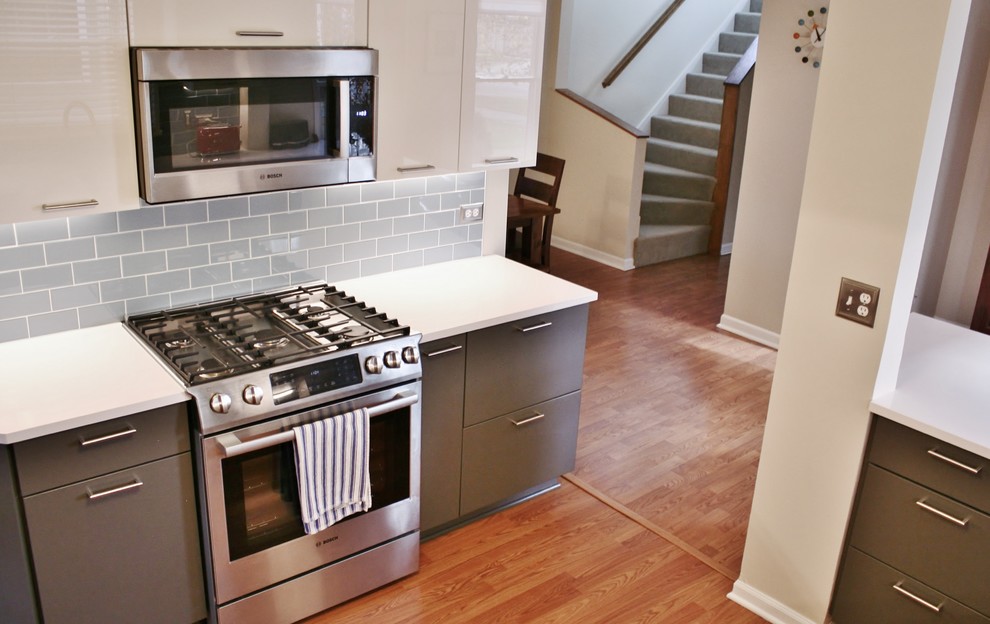 Example of a mid-sized minimalist u-shaped medium tone wood floor kitchen design with a farmhouse sink, flat-panel cabinets, gray cabinets, quartz countertops, blue backsplash, subway tile backsplash and colored appliances