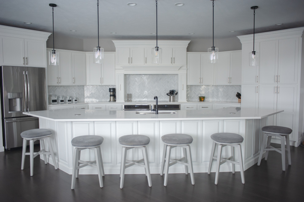 Design ideas for a large transitional galley kitchen in St Louis with an undermount sink, raised-panel cabinets, white cabinets, grey splashback, stainless steel appliances, dark hardwood floors, with island, brown floor and white benchtop.