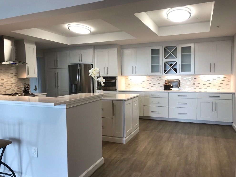 Large l-shaped eat-in kitchen in Other with shaker cabinets, white cabinets, stainless steel appliances, with island, brown floor and white benchtop.