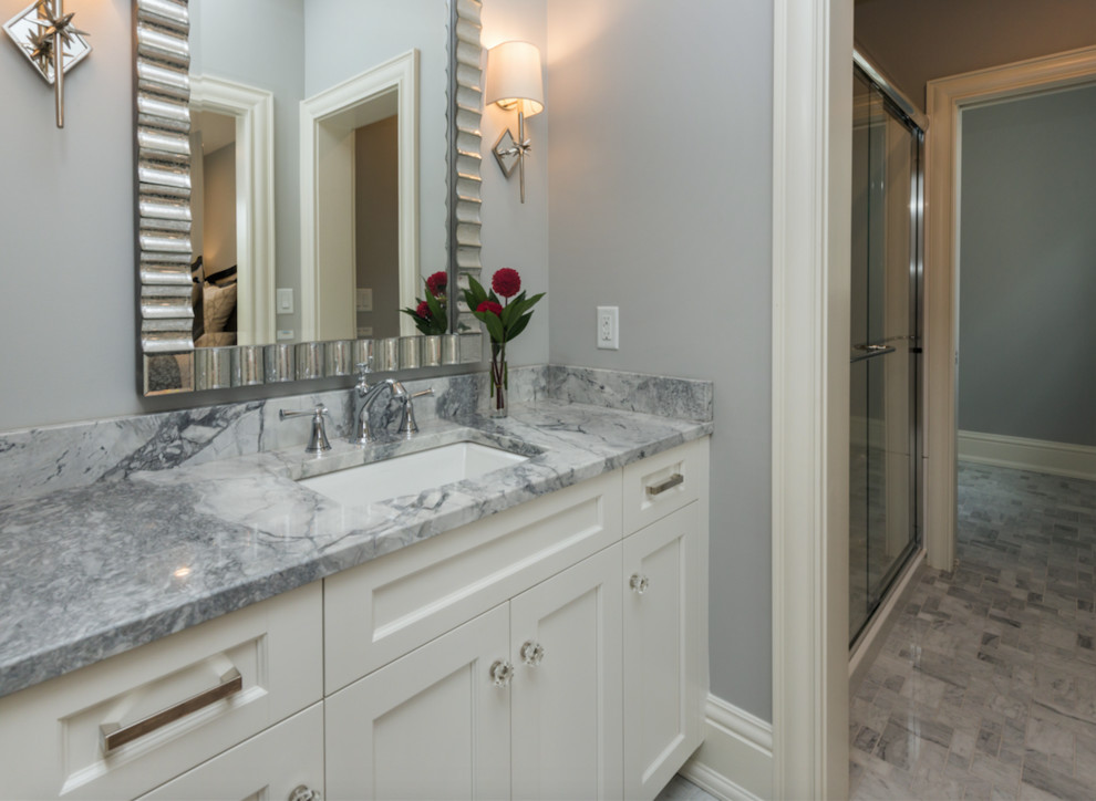 Mid-sized transitional gray tile and stone slab marble floor bathroom photo with recessed-panel cabinets, white cabinets, gray walls, a drop-in sink and granite countertops